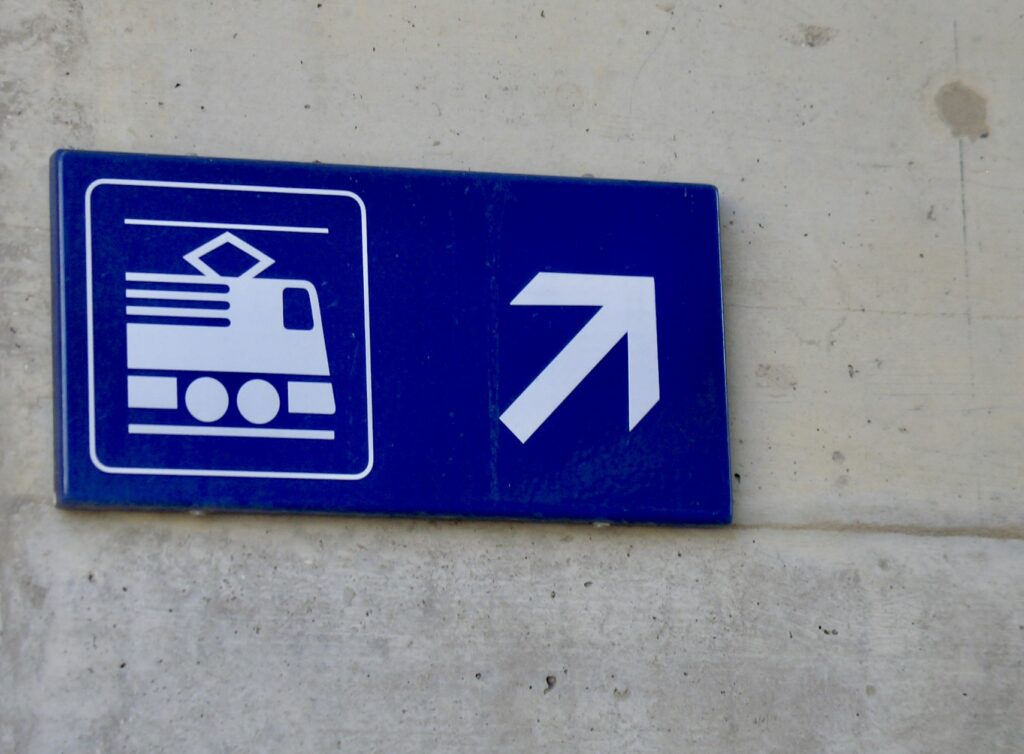 Blaues Bahnhofsschild mit Zugsymbol und Pfeil